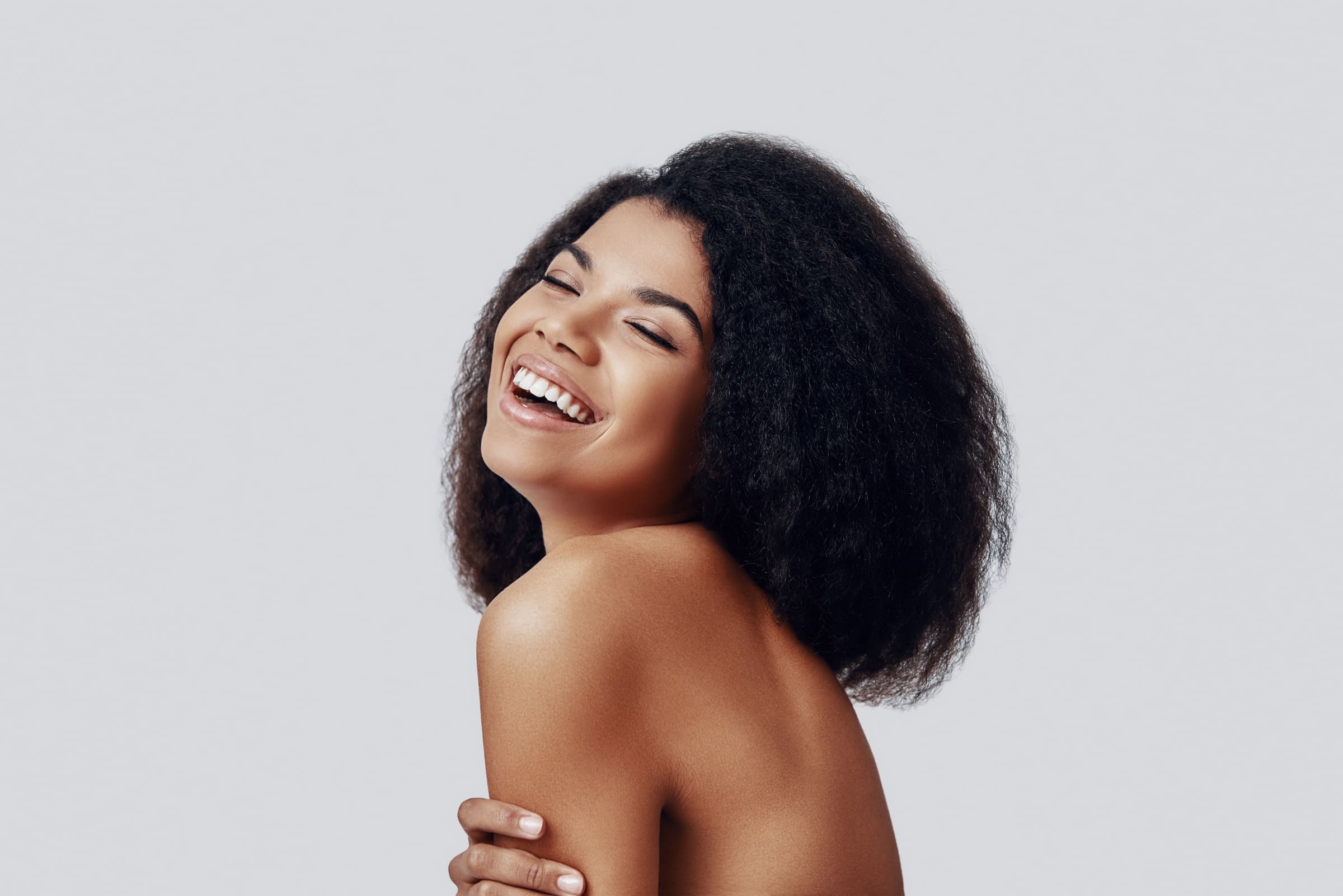Woman with curly hair laughing, eyes closed, against a light backdrop