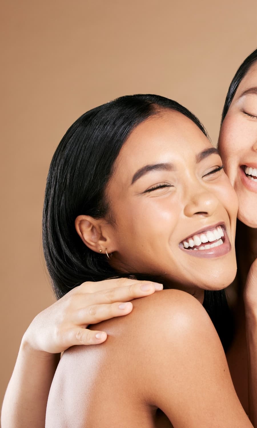 Two women laughing cheek to cheek against a warm backdrop