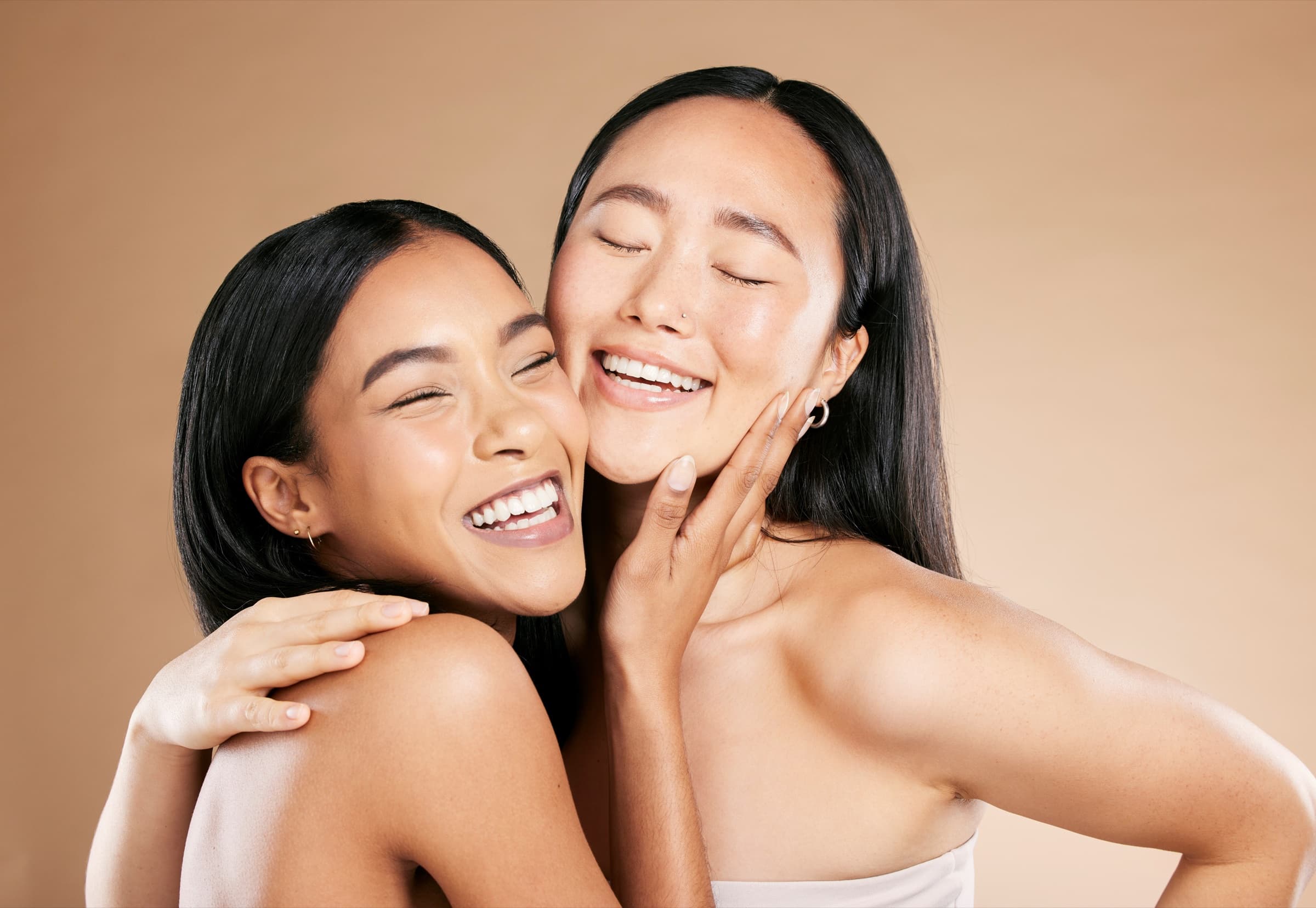 Two women laughing cheek to cheek against a warm backdrop