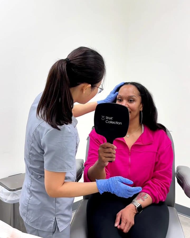 Rewind Bar provider assessing a patient’s face while the patient holds a hand mirror