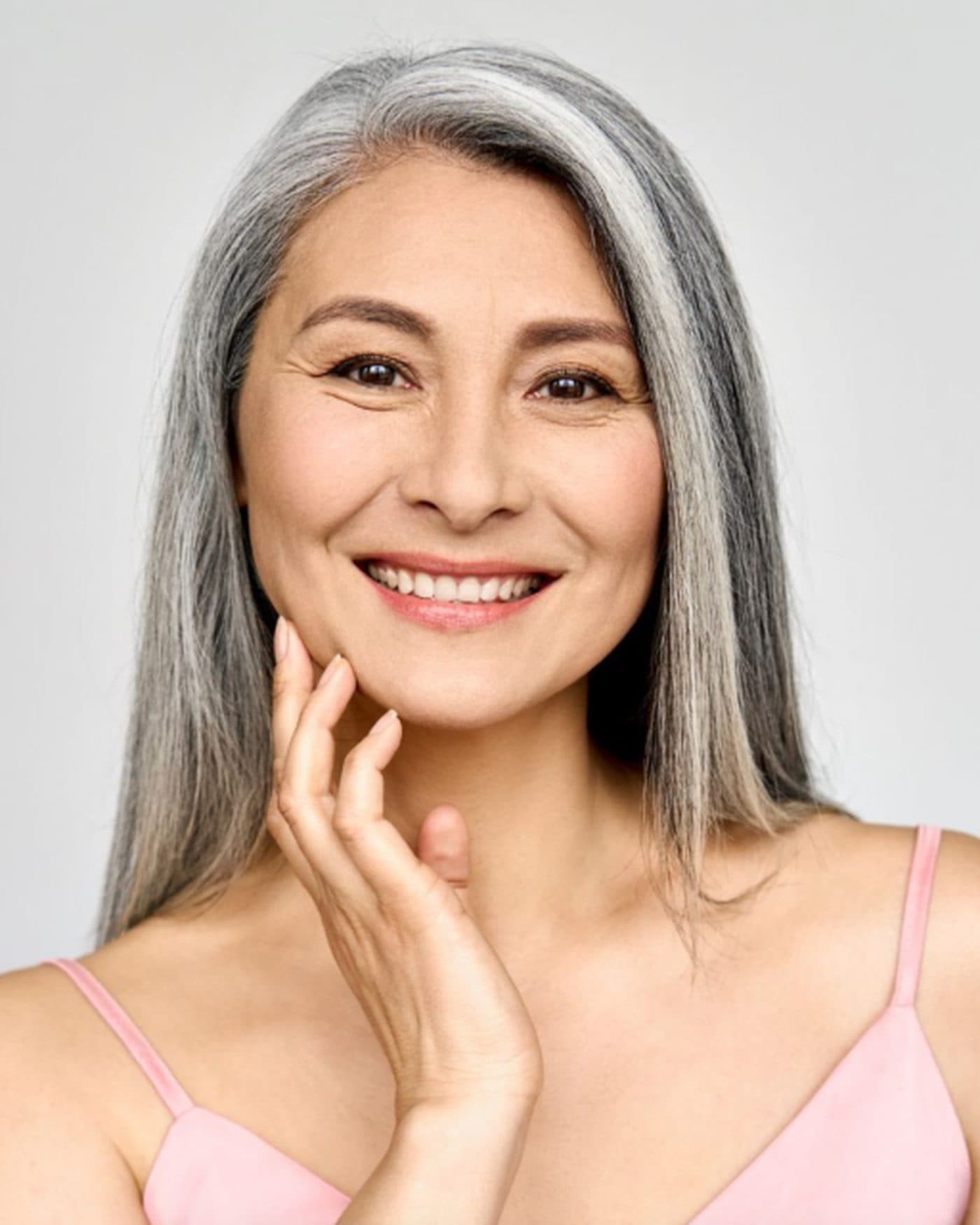 Woman with silver hair and clear, even skin resting her hand against her cheek